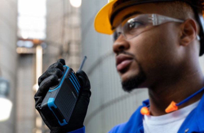 Man Holding Radio Outside Oil Plant 
