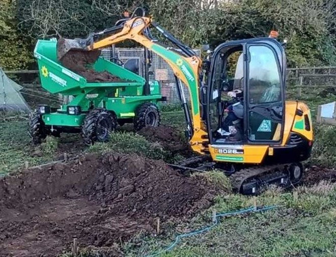 Mini Digger Unloading Dirt Into A Dumper On Patch Of Grass Worksite