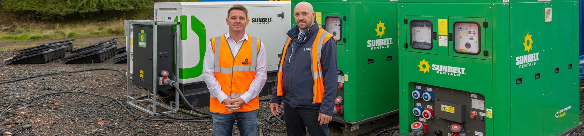 Two Project Managers Stood In front Of Battery Storage Units And A Hybrid Generator